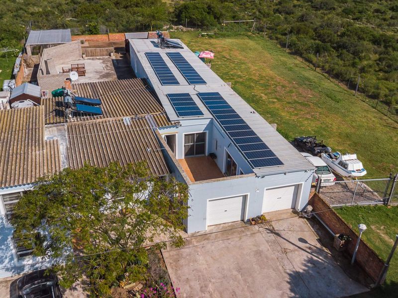 Aerial view of the property featuring a double garage, extensive solar panel installation, solar water heating system, and a concrete driveway.