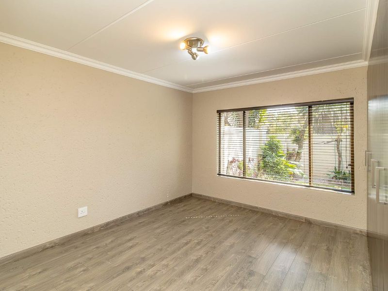 A bright, empty bedroom featuring modern laminate flooring, built-in cupboards, and venetian blinds overlooking the garden.