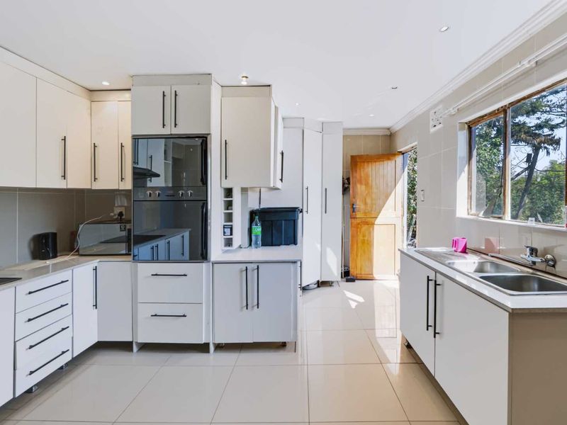 Modern kitchen featuring white cabinetry, built-in oven, extractor fan, double sink, and tiled flooring with natural light from the window and exterior door.