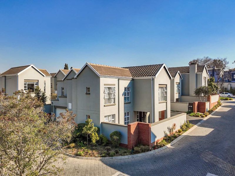 A well-maintained cluster home featuring a tiled roof, brick boundary walls, and a paved driveway within a secure residential estate.