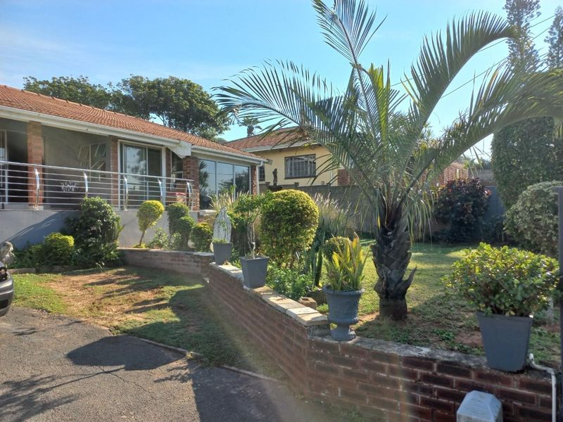 Front exterior view of the property featuring a brick retaining wall, landscaped garden, and a raised patio area with stainless steel balustrades.