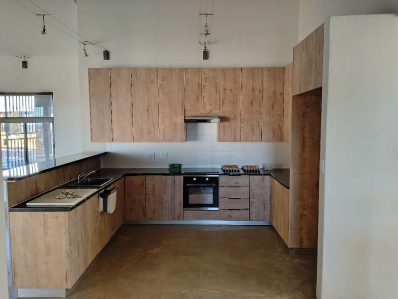 Modern kitchen featuring wood-look cabinetry, dark countertops, integrated appliances, and a functional layout with a breakfast bar and track lighting.