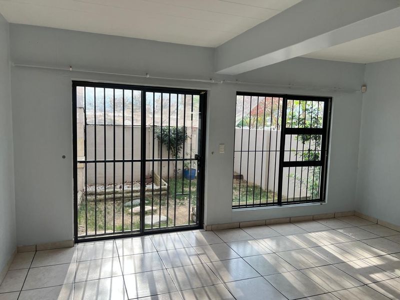 An empty living area featuring tiled flooring, large sliding glass doors with security bars, and direct access to an outdoor space.