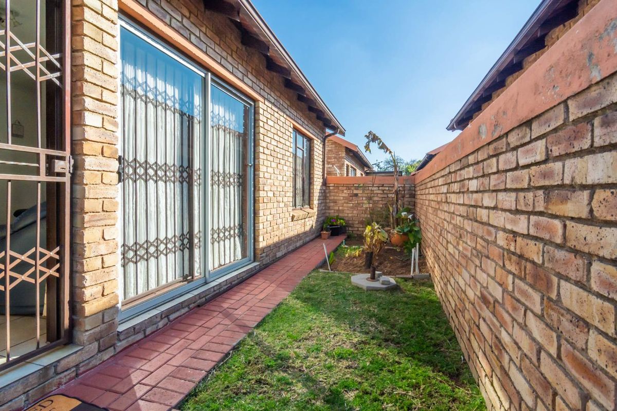 A side garden area featuring a paved walkway, exposed brick exterior walls, and a secure sliding door entrance with metal security gate.