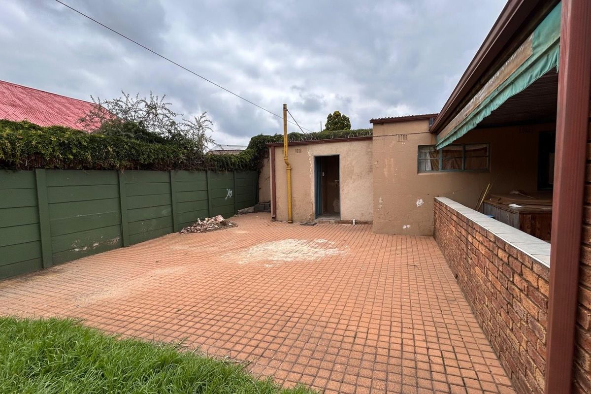 A paved rear courtyard area featuring a brick boundary wall, perimeter fencing, and access to a secondary utility structure.