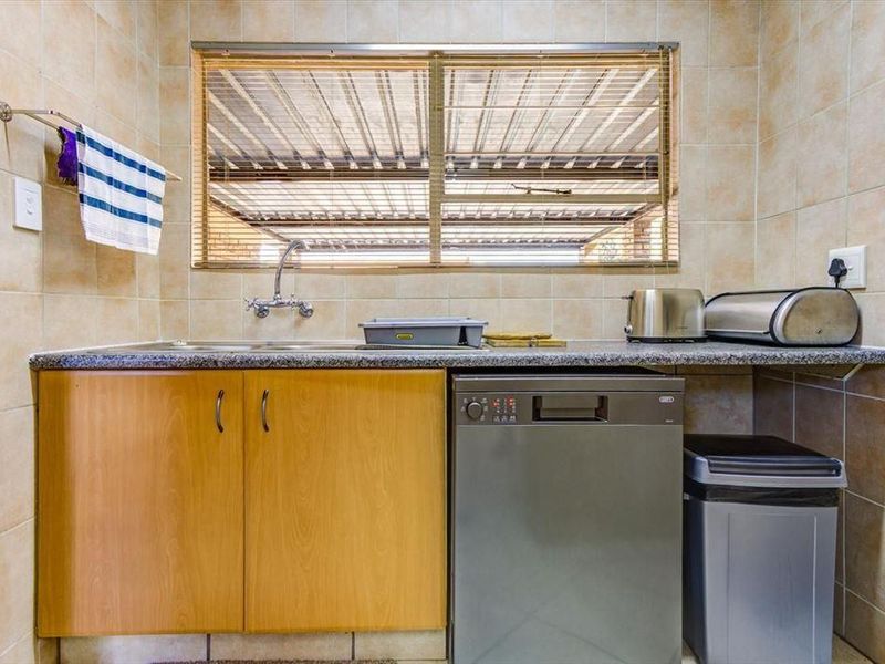 A functional scullery area featuring built-in wooden cabinetry, granite countertops, a stainless steel sink, and tiled wall finishes.