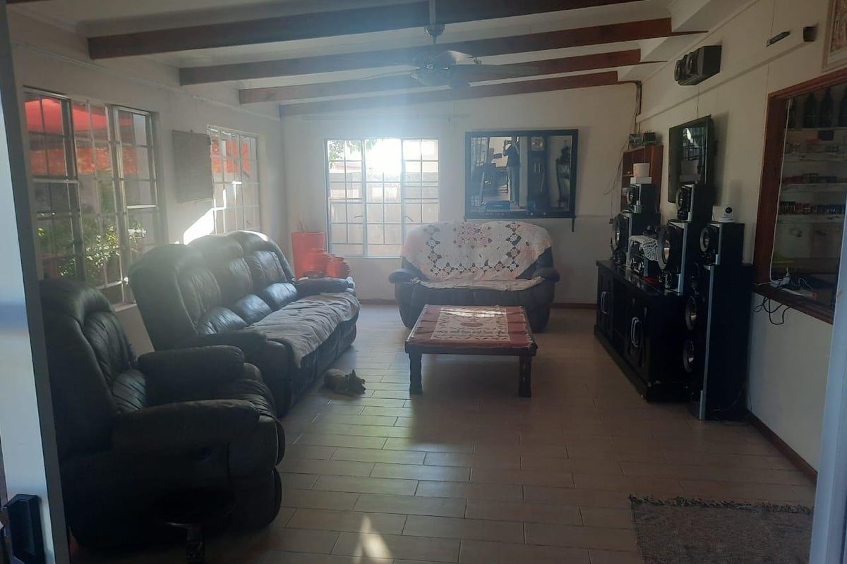 Spacious living room featuring exposed timber ceiling beams, tiled flooring, and large windows providing natural light.