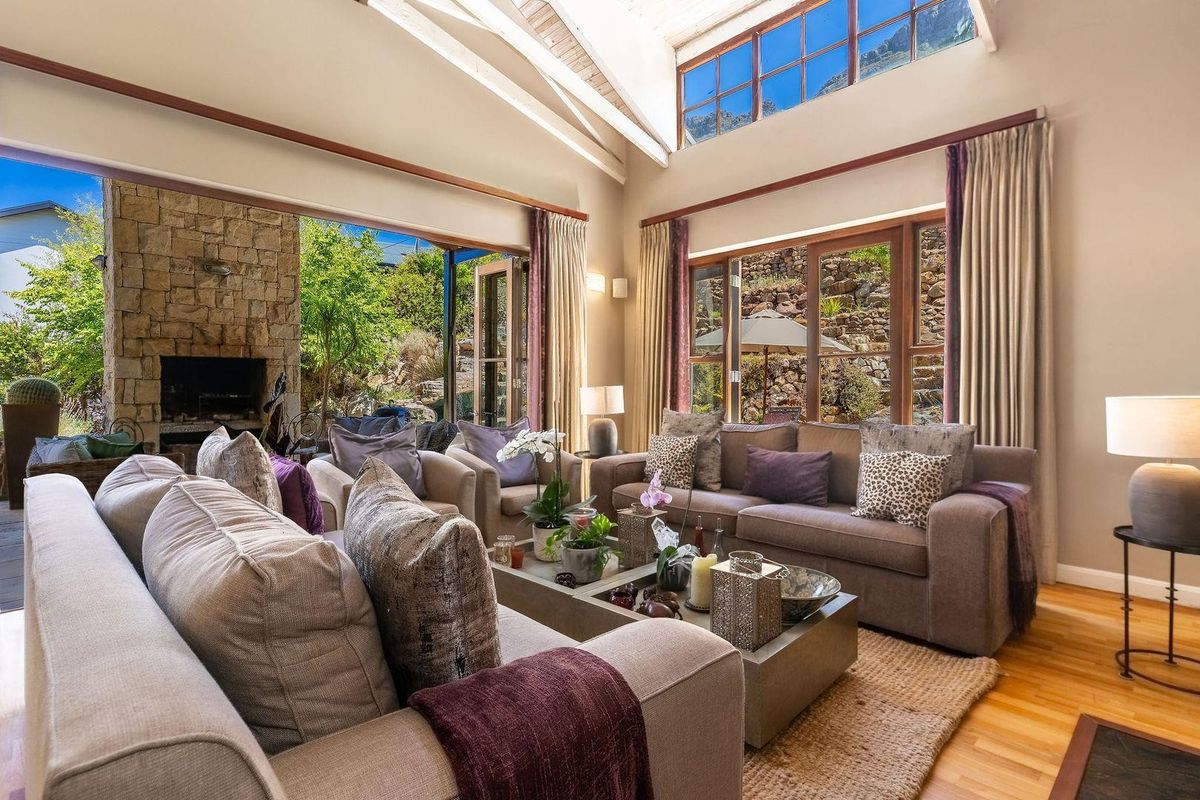 Spacious living room featuring vaulted ceilings, exposed timber beams, large windows, and seamless indoor-outdoor flow to a stone-clad fireplace patio.