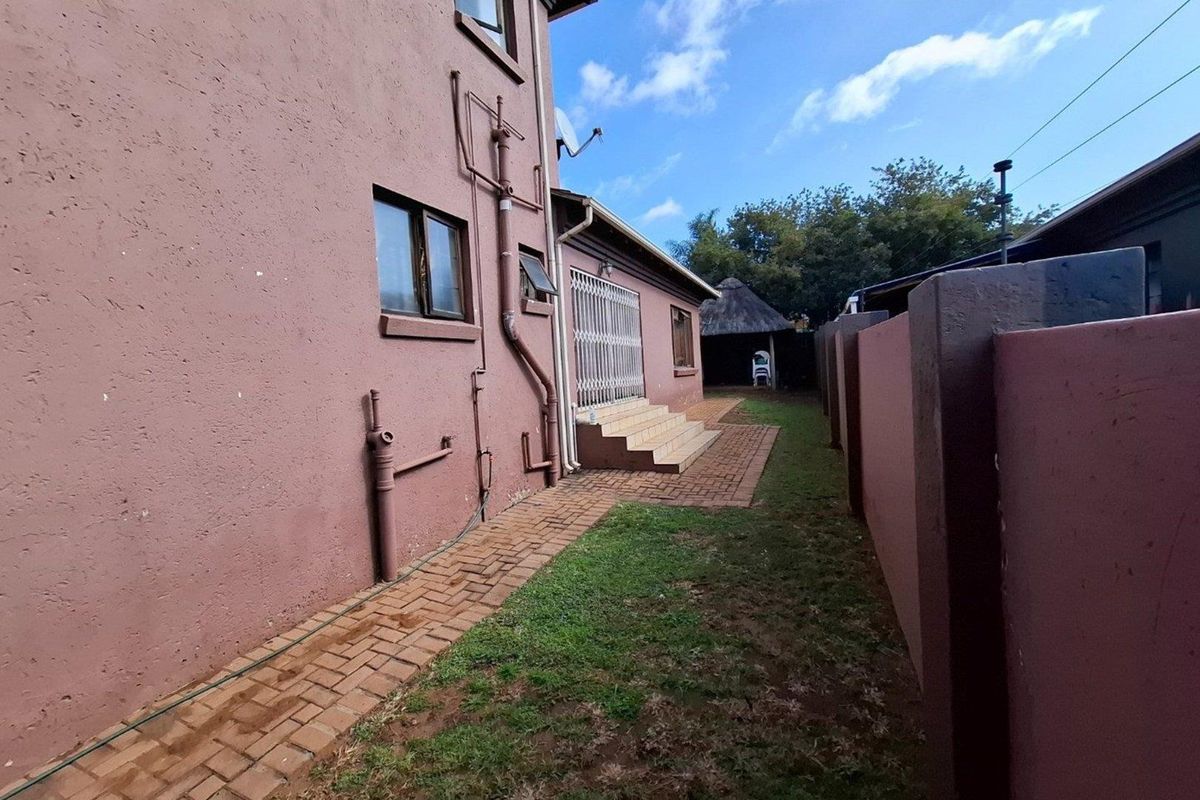 Rear exterior view of the property featuring a paved walkway, boundary wall, and security gate access to the main building.