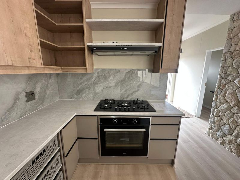 Modern kitchen featuring a gas hob, built-in oven, extractor fan, stone-look splashback, and contemporary cabinetry, adjacent to a unique stone feature wall.