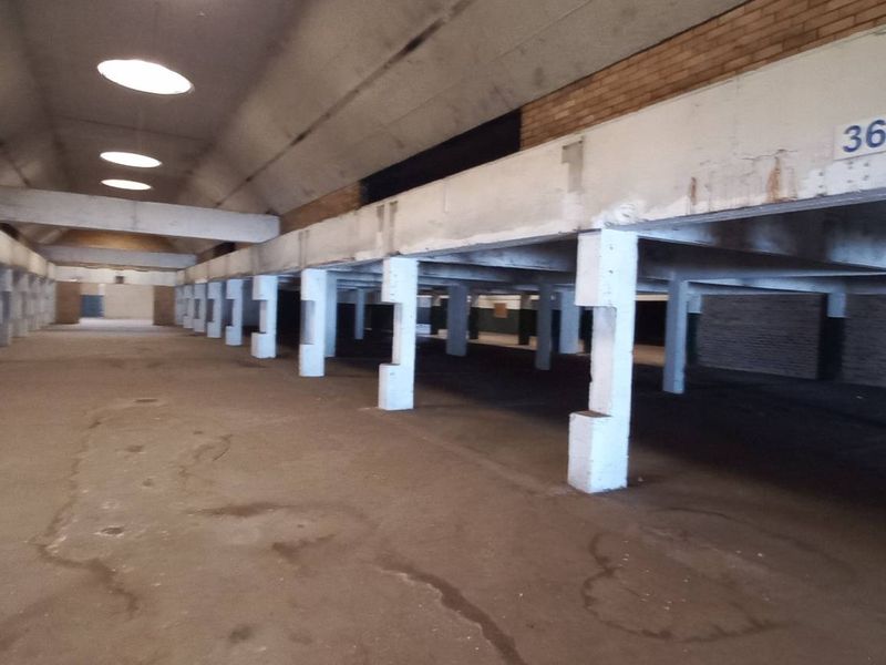 Expansive industrial warehouse space featuring high vaulted ceilings, exposed brickwork, and a series of structural concrete support columns throughout the open floor plan.