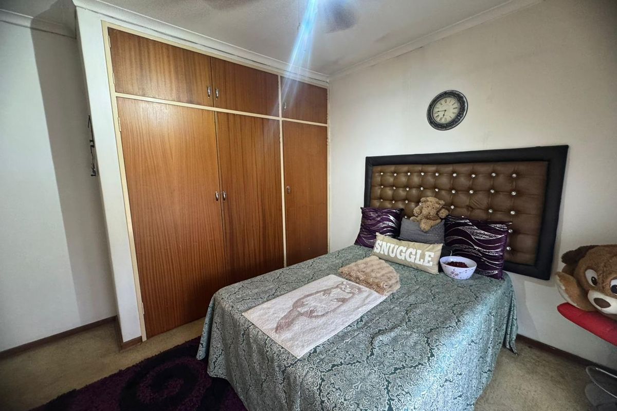 A bedroom featuring built-in wooden wardrobes and a ceiling fan, offering a functional space with neutral wall finishes.