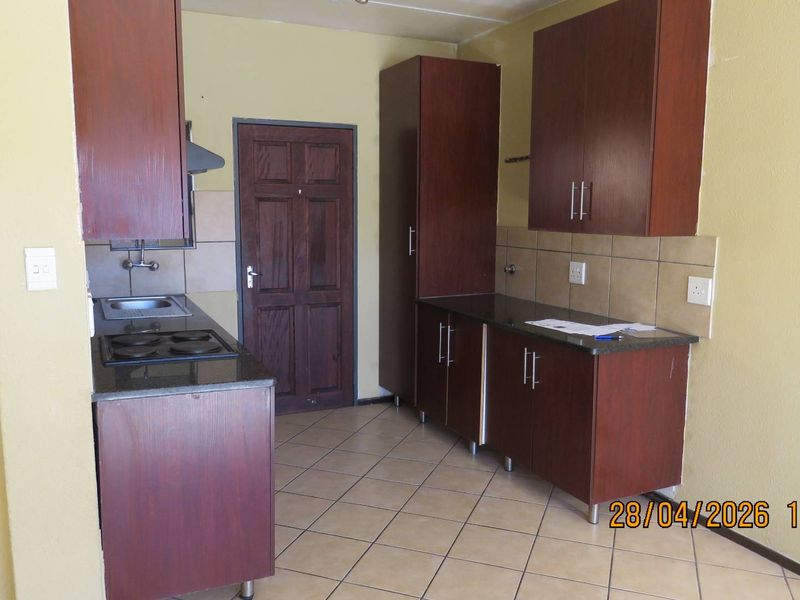 A functional kitchen featuring dark wood cabinetry, granite countertops, a built-in electric hob, and tiled flooring, offering a practical layout for daily use.