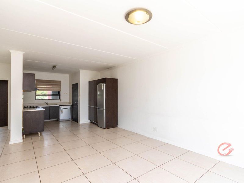 An open-plan living and kitchen area featuring tiled flooring, modern dark cabinetry, and integrated kitchen appliances in a clean, neutral space.