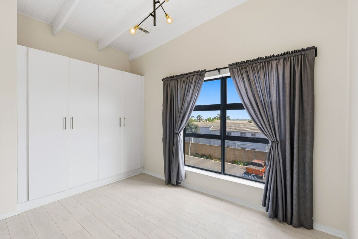 Bright bedroom featuring vaulted ceilings with exposed beams, built-in cupboards, modern laminate flooring, and a large window with views.