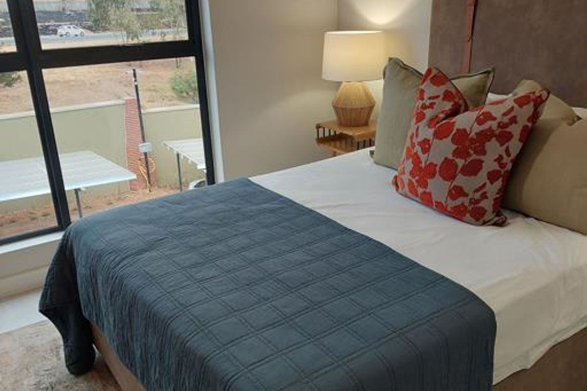 A well-lit bedroom featuring large windows with exterior views and neutral wall finishes.