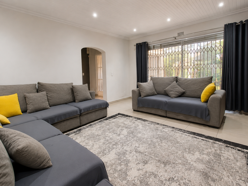 A well-maintained living room featuring tiled floors, recessed downlighting, a distinctive tongue and groove ceiling, and an arched entryway leading to adjacent spaces.