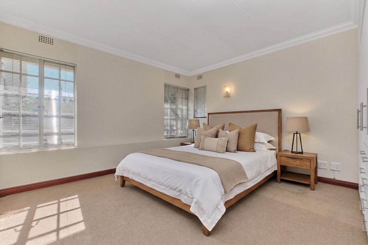 A well-maintained bedroom featuring neutral carpeting, built-in cupboards, and natural light through venetian blinds.