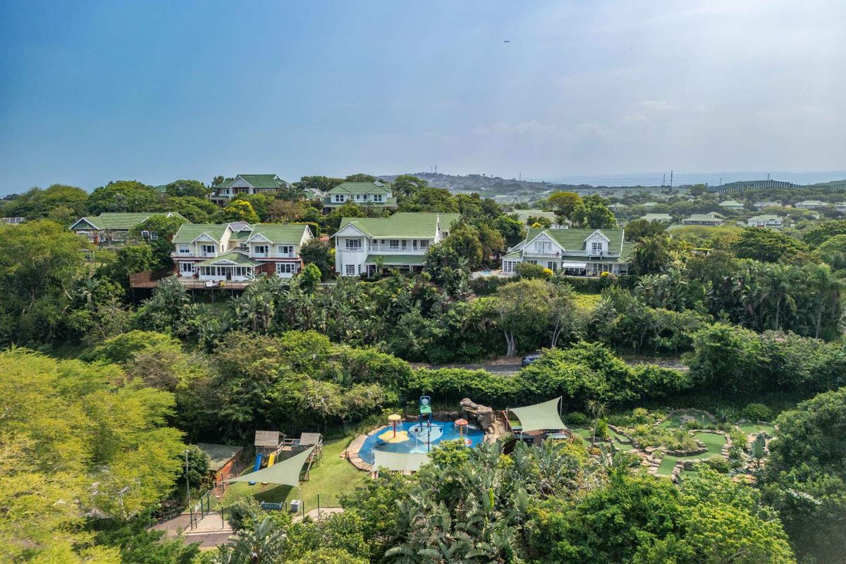 Aerial view of a residential estate featuring multiple homes, a swimming pool, playground, and lush landscaped surroundings.