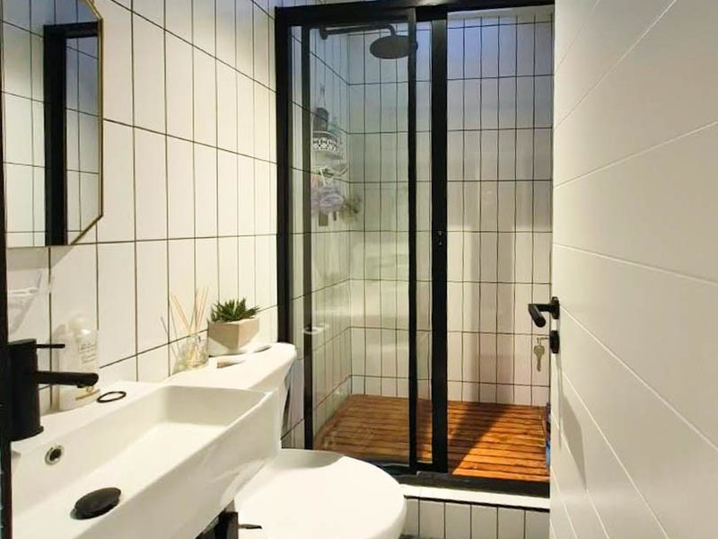 Modern bathroom featuring a wall-mounted vanity with black fixtures, a tiled shower enclosure with a black frame, and a skylight for natural illumination.