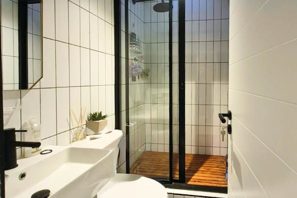 Modern bathroom featuring a wall-mounted vanity with black fixtures, a tiled shower enclosure with a black frame, and a skylight for natural illumination.