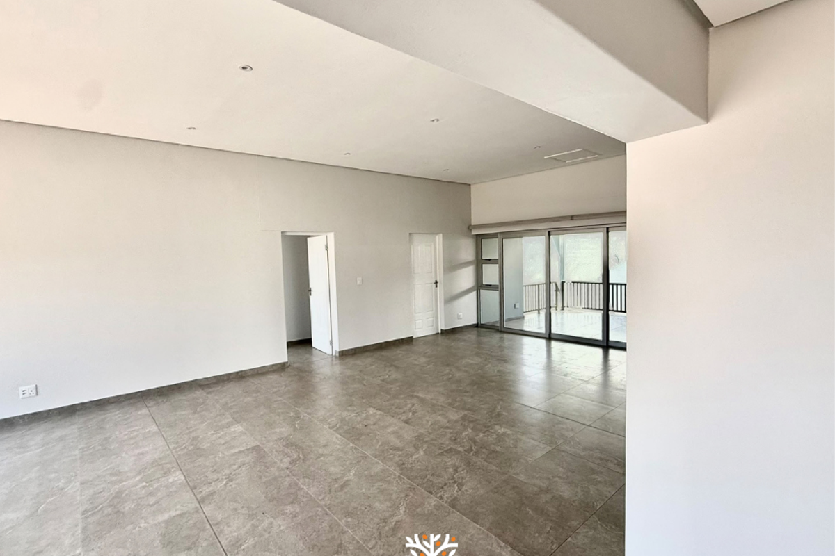 Spacious, modern open-plan living area featuring large format floor tiles, recessed lighting, and seamless access to an outdoor balcony through sliding glass doors.