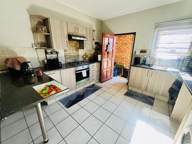 Functional kitchen featuring light wood-grain cabinetry, granite countertops, gas hob, electric oven, and tiled flooring with direct access to an outdoor area.