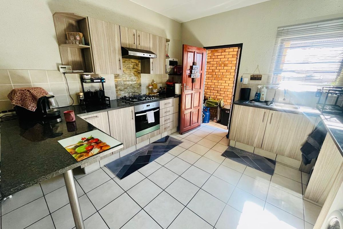 Functional kitchen featuring light wood-grain cabinetry, granite countertops, gas hob, electric oven, and tiled flooring with direct access to an outdoor area.