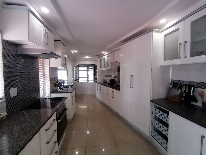 Modern galley-style kitchen featuring white cabinetry, granite countertops, integrated appliances, mosaic backsplash, and polished tile flooring with recessed lighting.