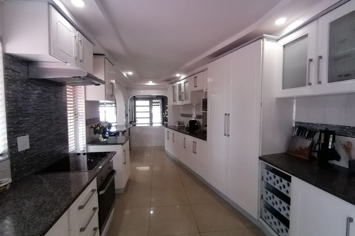 Modern galley-style kitchen featuring white cabinetry, granite countertops, integrated appliances, mosaic backsplash, and polished tile flooring with recessed lighting.