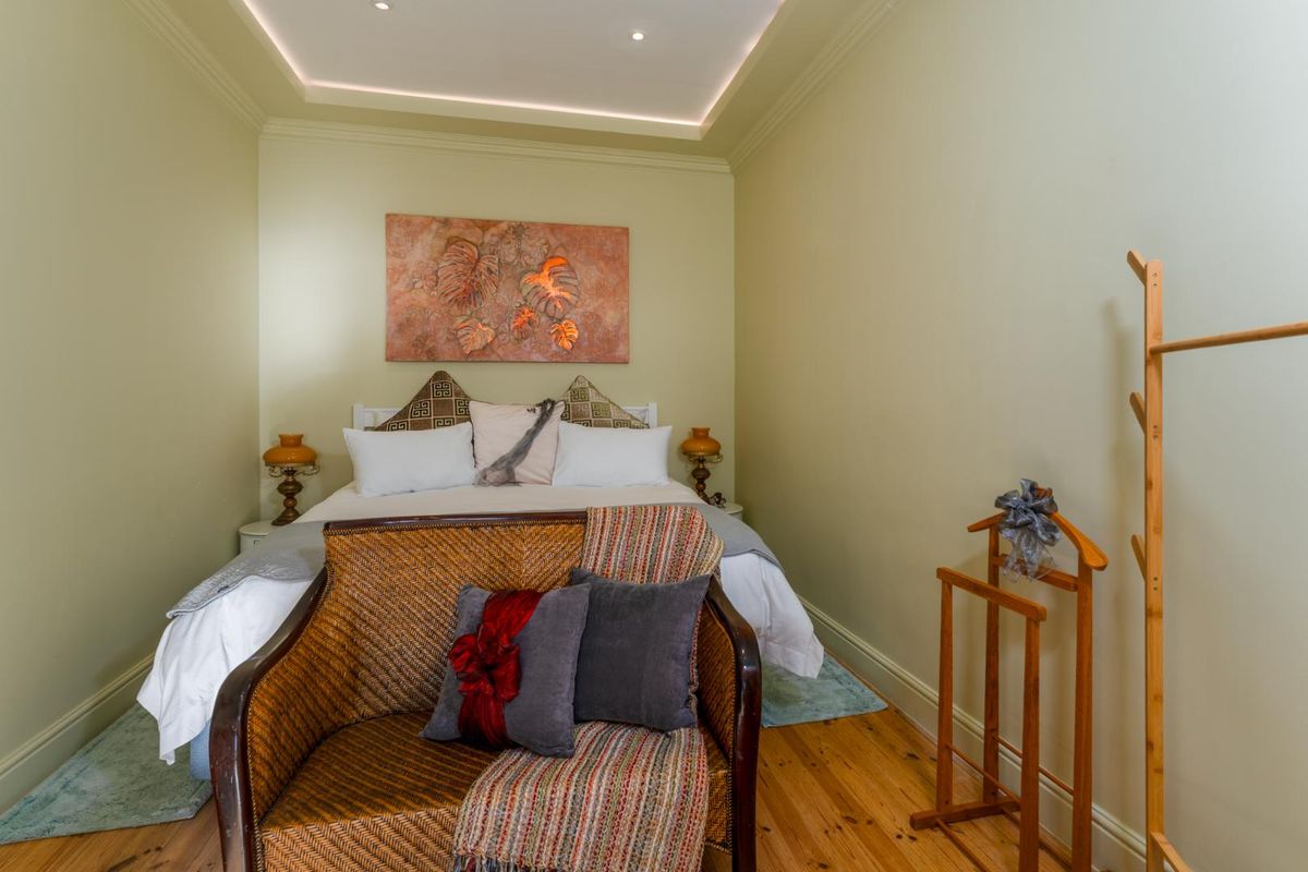 A cozy bedroom featuring warm-toned timber flooring, recessed ceiling lighting with coving, and neutral wall finishes.