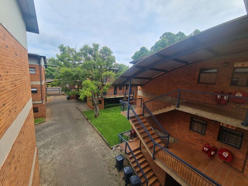 An elevated view of an apartment complex courtyard featuring brick buildings, external metal staircases, paved walkways, and landscaped green space.