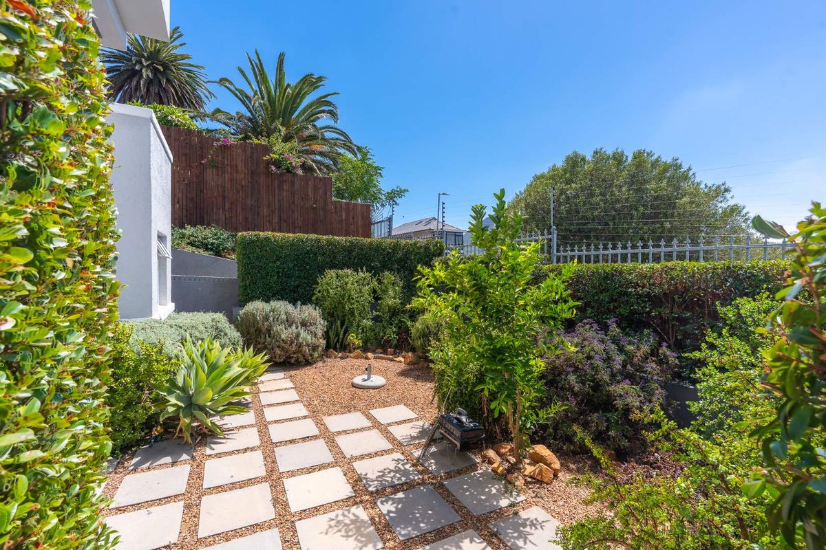 A well-maintained rear garden area featuring paved pathways, gravel landscaping, established hedging, and secure perimeter fencing.