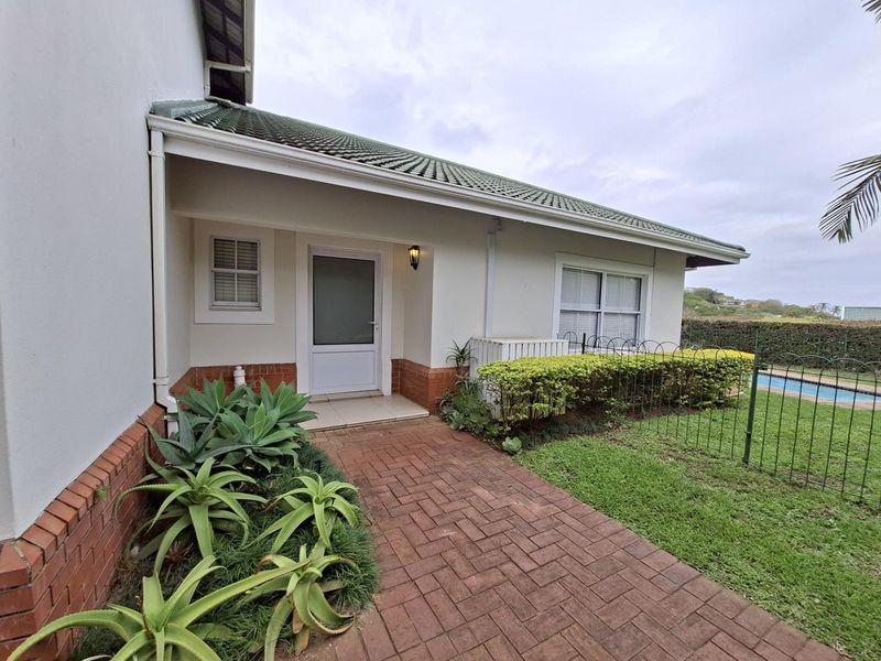 A well-maintained townhouse entrance featuring a brick-paved walkway, tiled roof, and landscaped garden area with metal fencing.