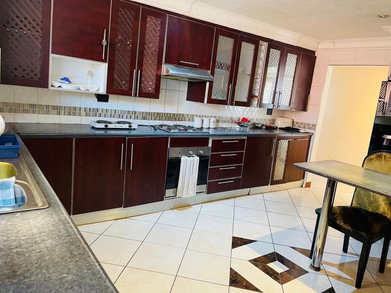 A functional kitchen featuring dark wood cabinetry, built-in oven, gas hob, extractor fan, and tiled flooring with a decorative inlay.
