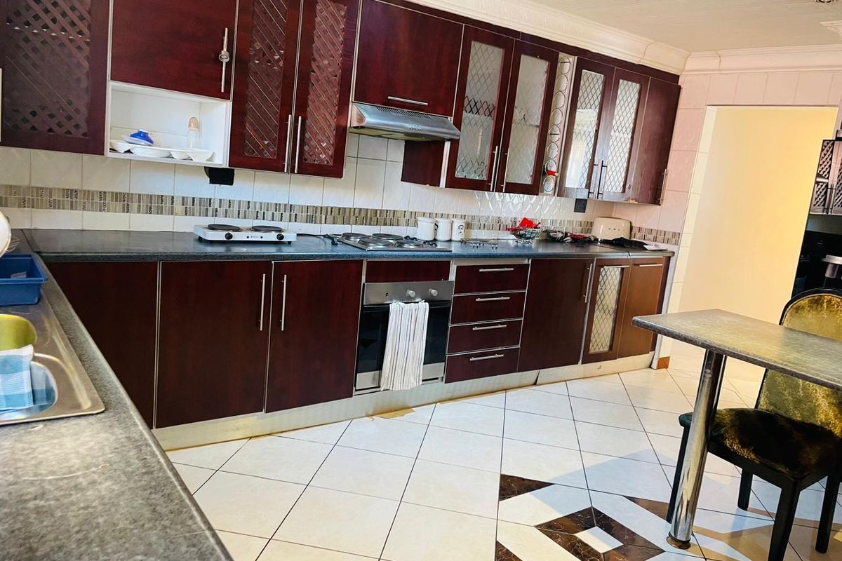 A functional kitchen featuring dark wood cabinetry, built-in oven, gas hob, extractor fan, and tiled flooring with a decorative inlay.
