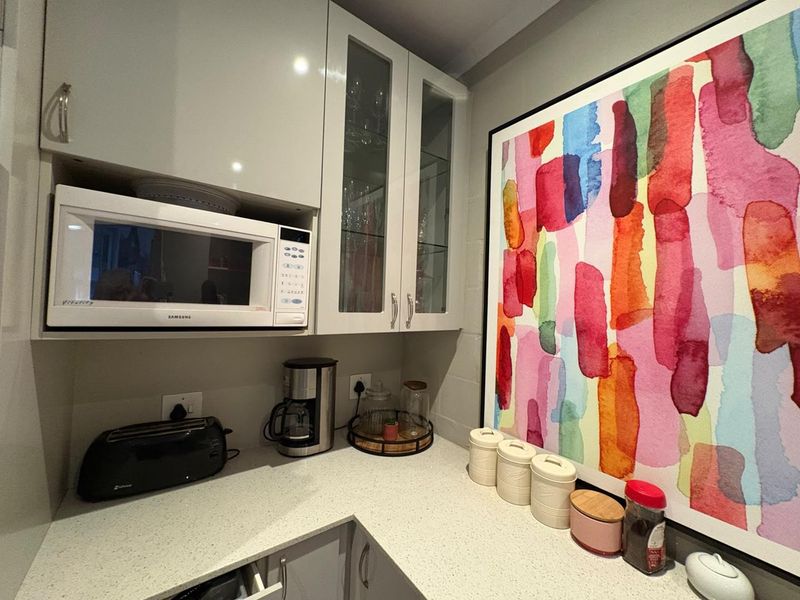 A modern kitchen corner featuring high-gloss cabinetry, glass-fronted display cupboards, and a durable quartz countertop with integrated microwave.