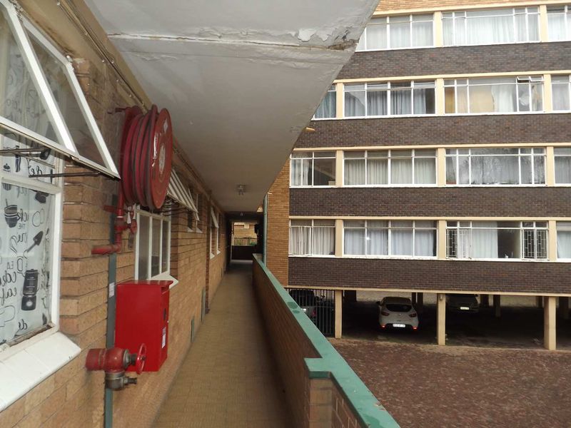 Exterior walkway of an apartment building featuring brick facade, fire safety equipment, and views of the parking area.