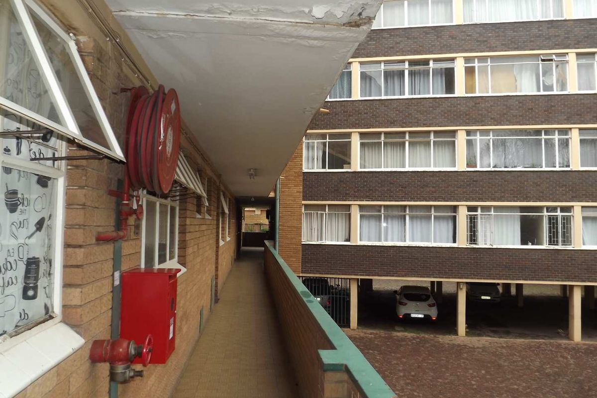 Exterior walkway of an apartment building featuring brick facade, fire safety equipment, and views of the parking area.