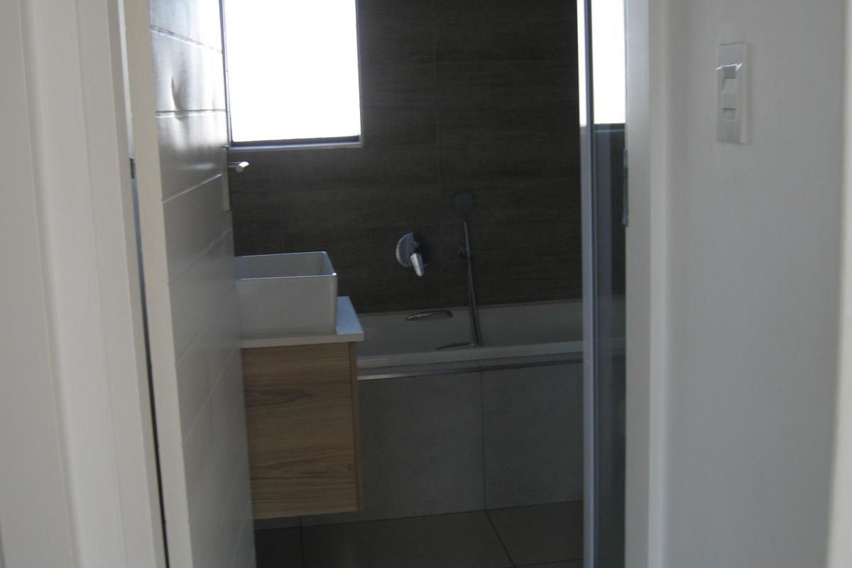 A modern bathroom featuring a floating vanity with a vessel sink, a bathtub with a wall-mounted mixer, and dark tiled feature walls.