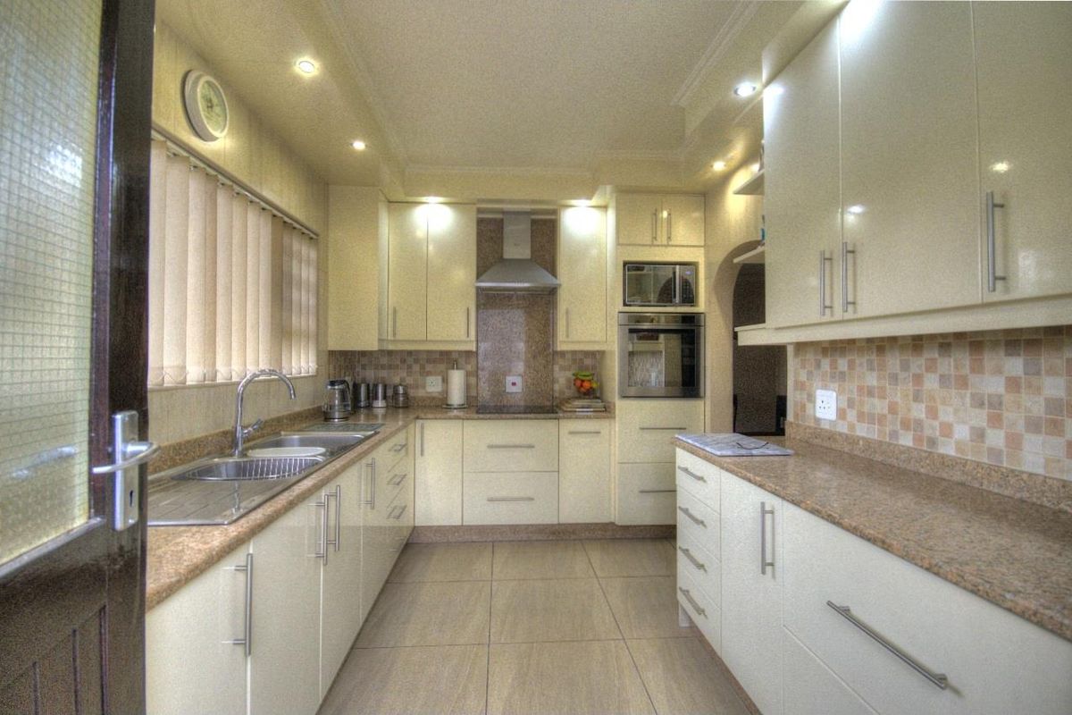 A well-maintained kitchen featuring cream cabinetry, granite countertops, tiled backsplash, built-in oven, extractor fan, and recessed ceiling lighting.