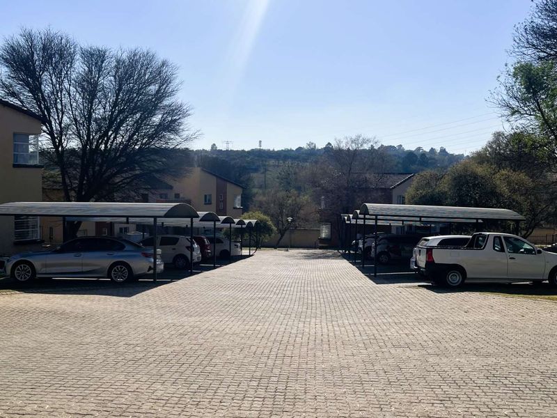 Exterior view of the townhouse complex featuring a paved driveway and covered carport parking bays for residents.