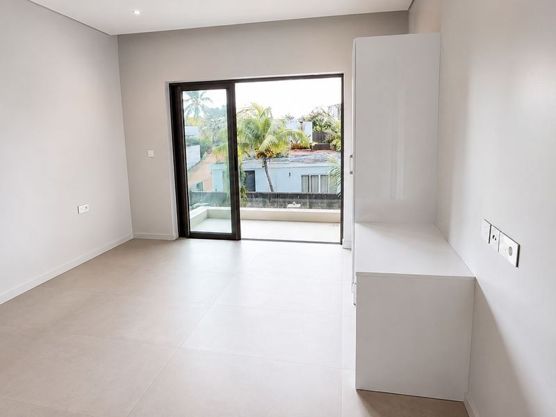 A bright, modern, and empty bedroom featuring neutral tiled flooring, built-in cabinetry, and a sliding glass door leading to a private balcony.