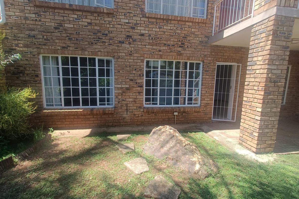 Rear view of a face brick townhouse featuring grid-pattern windows, a security gate, and a small garden area with a covered patio above.