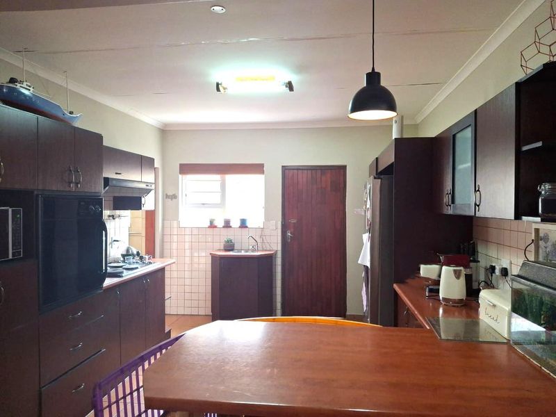 Functional kitchen featuring dark wood cabinetry, laminate countertops, built-in oven, extractor fan, and tiled backsplash with a practical layout.