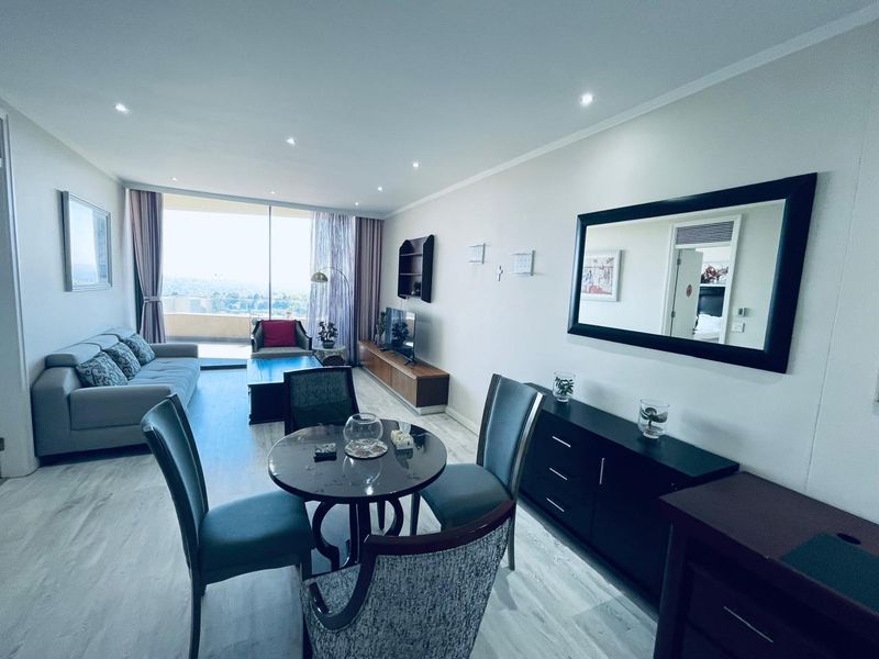 Open-plan living and dining area featuring modern laminate flooring, recessed lighting, and large sliding glass doors leading to a balcony with expansive views.