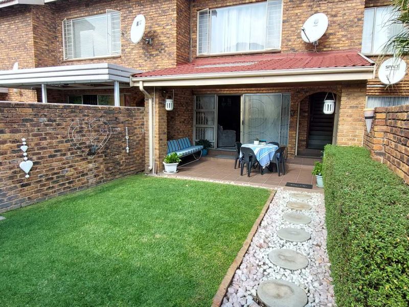 A private rear garden featuring a paved patio area, a small lawn, and a stone-paved pathway, set against the brick facade of the townhouse.
