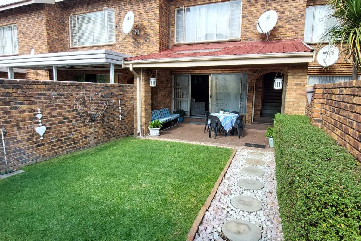 A private rear garden featuring a paved patio area, a small lawn, and a stone-paved pathway, set against the brick facade of the townhouse.