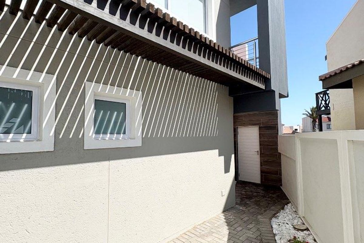 Side exterior view of the townhouse featuring paved walkway, decorative timber pergola, and modern facade finishes.