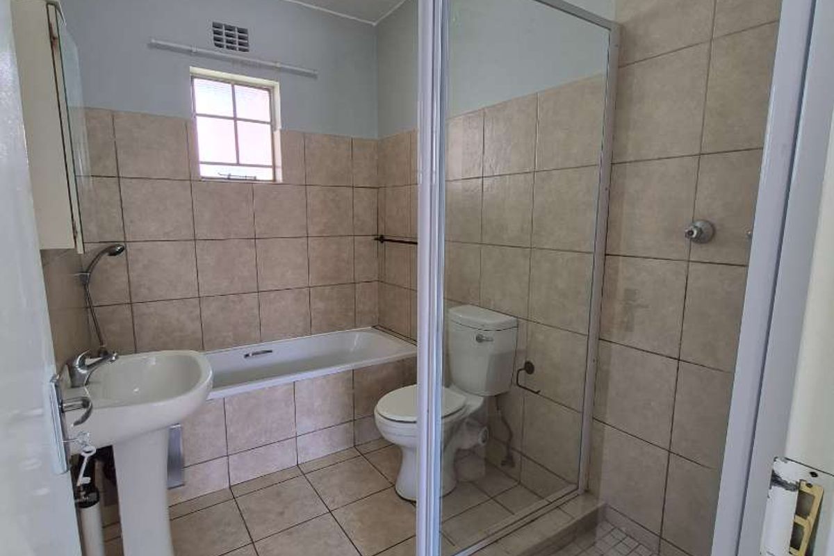 A functional bathroom featuring a pedestal basin, bathtub, and a separate glass-enclosed shower with neutral wall and floor tiling.